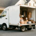 Camion de déménagement garé devant une maison, avec des cartons, des clés et des objets domestiques soigneusement organisés.