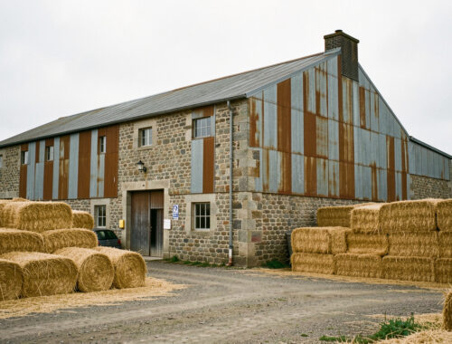 Ancien bâtiment industriel reconverti à Lampaul-Guimiliau, entouré de balles de paille de lin dans une ambiance documentaire bretonne.
