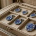 Bijoux artisanaux en faïence ancienne, comprenant des boucles d’oreilles et des pendentifs aux motifs bleus, disposés dans un écrin de voyage en tissu posé sur une valise cabine.